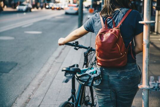 Photo d'un cycliste tenant son vélo à la main sur un trottoir.